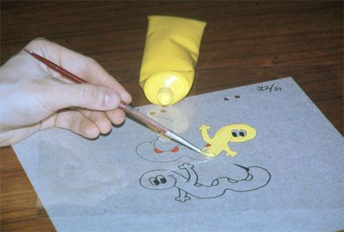 A hand painting colour onto the back of a transparent animation cel