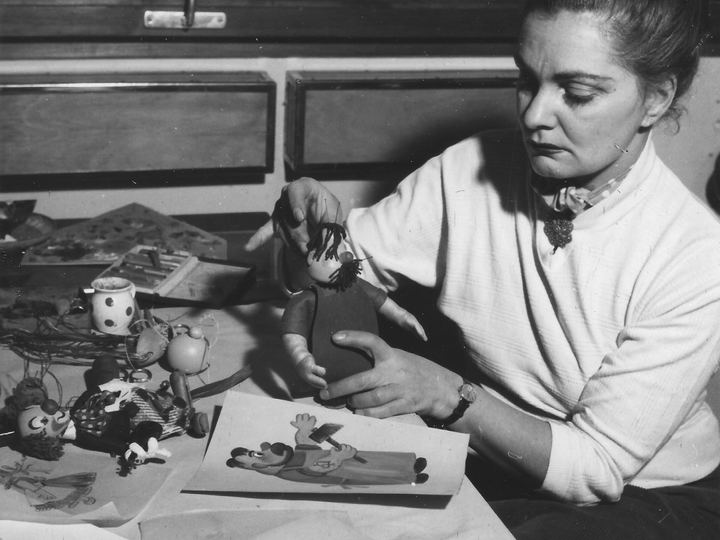 Filmmaker Éva Balla-Falus posing small puppets on a table in a puppet animation studio in 1955